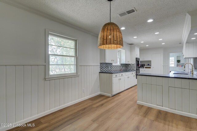 4013 48th St, Lubbock, TX 79413 - kitchen featuring dark countertops, wainscoting, a textured ceiling, white cabinetry, and light wood-style flooring
