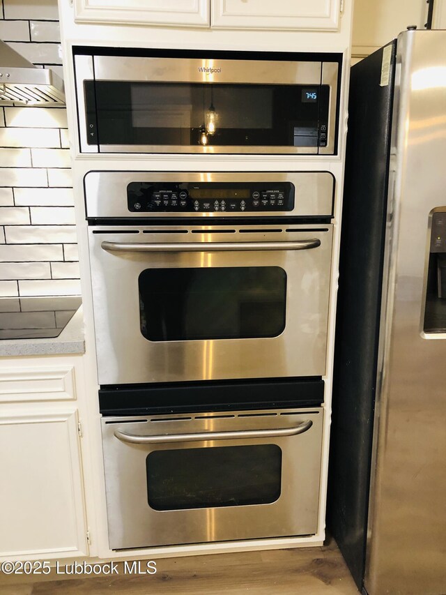 5712 73rd St, Lubbock, TX 79424 - kitchen with stainless steel appliances, light countertops, white cabinets, wood finished floors, and exhaust hood