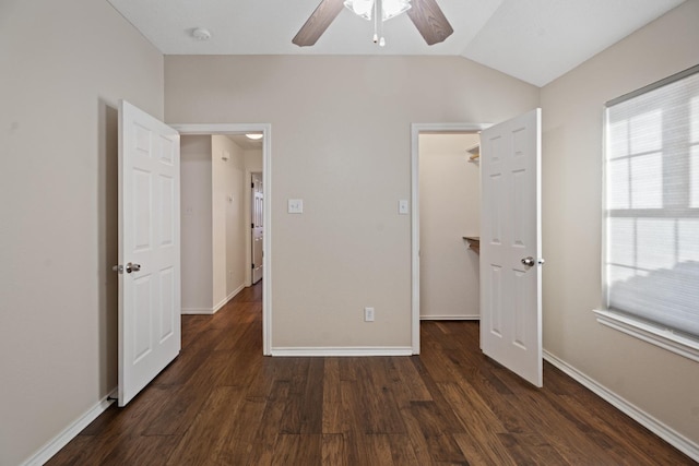 unfurnished bedroom featuring a spacious closet, dark wood-type flooring, ceiling fan, and vaulted ceiling