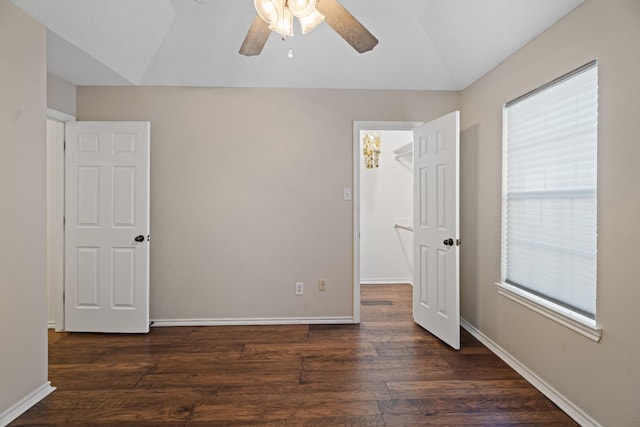 unfurnished bedroom with vaulted ceiling, a walk in closet, dark wood-type flooring, and ceiling fan