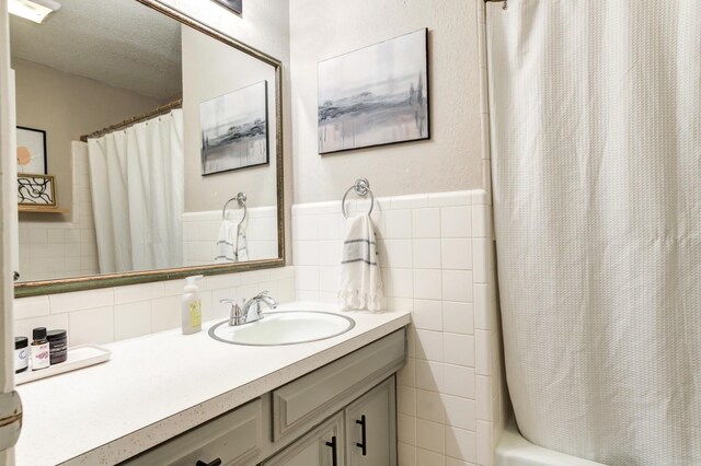 bathroom featuring vanity, tile walls, shower / tub combo with curtain, and a textured ceiling