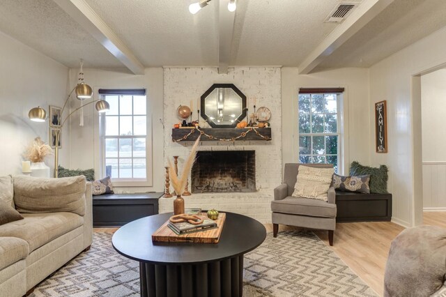 living room with light hardwood / wood-style flooring, beam ceiling, a fireplace, and a textured ceiling