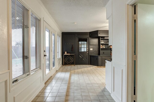 hallway with ornamental molding, a textured ceiling, and light tile patterned flooring