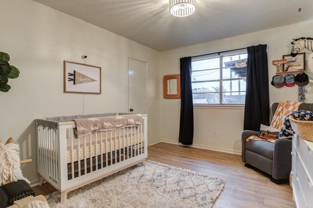 bedroom featuring a crib, a textured ceiling, and light wood-type flooring