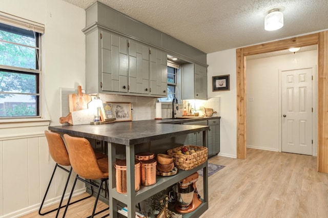 kitchen with sink, a textured ceiling, light hardwood / wood-style floors, and decorative backsplash