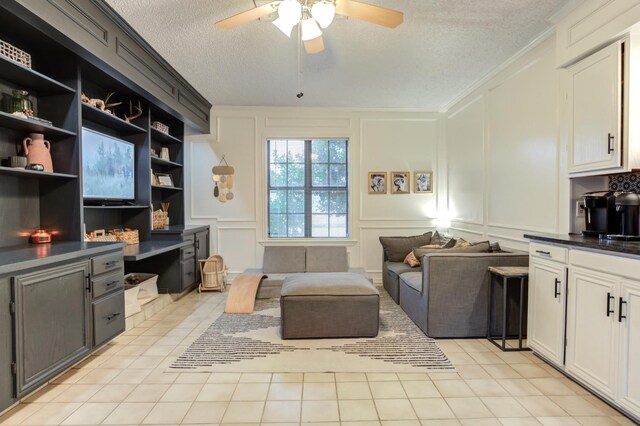 living room featuring ceiling fan, light tile patterned floors, ornamental molding, and a textured ceiling