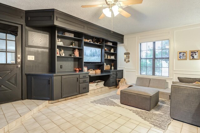 interior space with light tile patterned flooring, ceiling fan, built in desk, and a textured ceiling