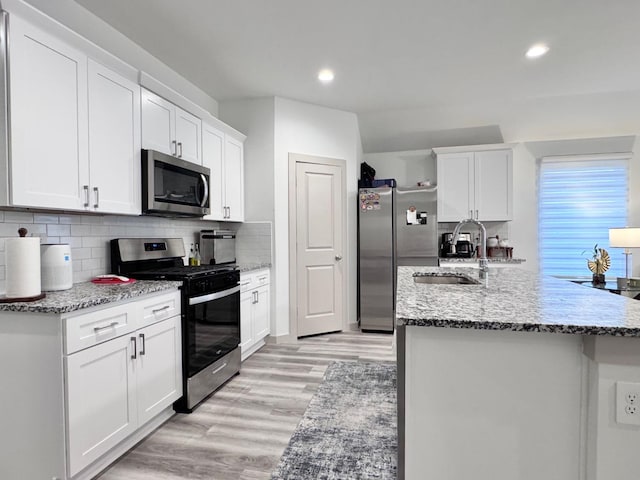 kitchen with light stone countertops, appliances with stainless steel finishes, sink, and white cabinets