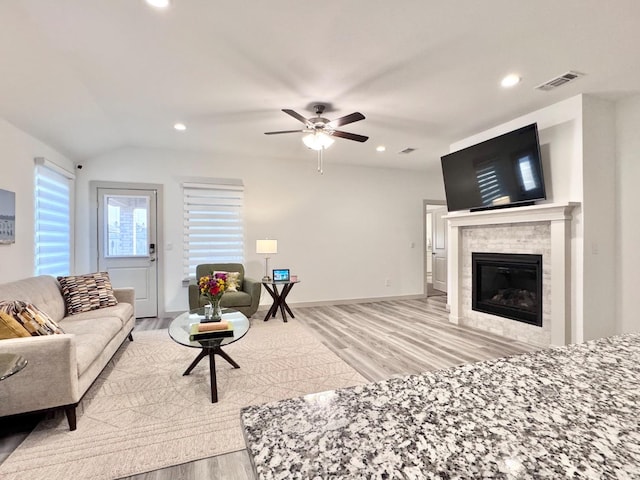 living room with a tiled fireplace, lofted ceiling, ceiling fan, and light hardwood / wood-style flooring