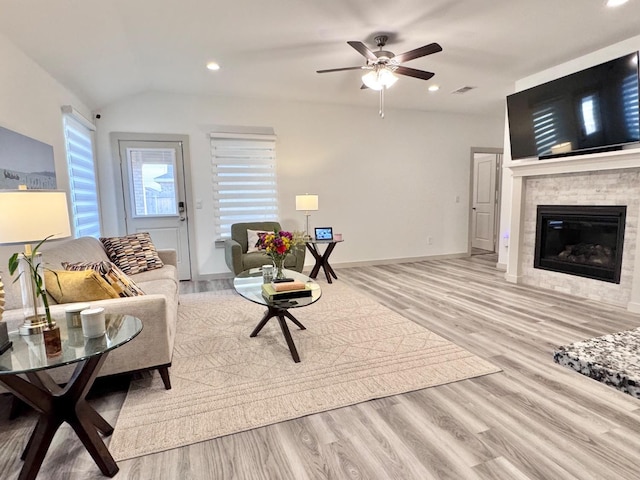 living room featuring a tiled fireplace, lofted ceiling, ceiling fan, and light wood-type flooring