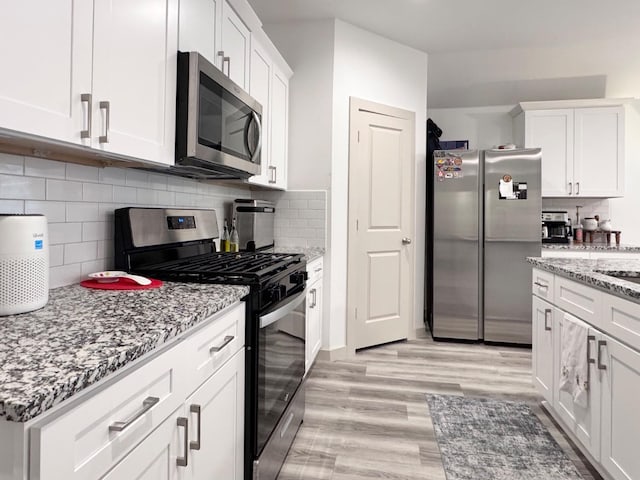 kitchen with appliances with stainless steel finishes, backsplash, white cabinets, light stone counters, and light wood-type flooring