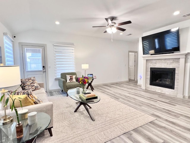 living room featuring a tiled fireplace, vaulted ceiling, ceiling fan, and light hardwood / wood-style flooring