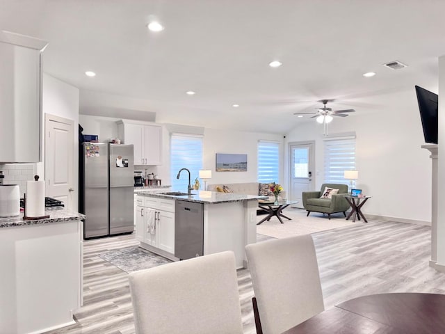 kitchen with an island with sink, appliances with stainless steel finishes, white cabinets, and light stone counters