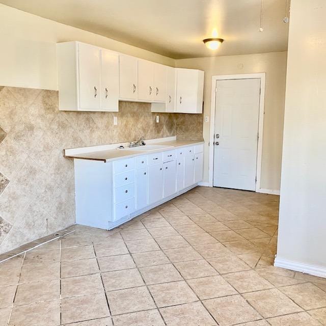 kitchen with white cabinetry, backsplash, sink, and light tile patterned floors