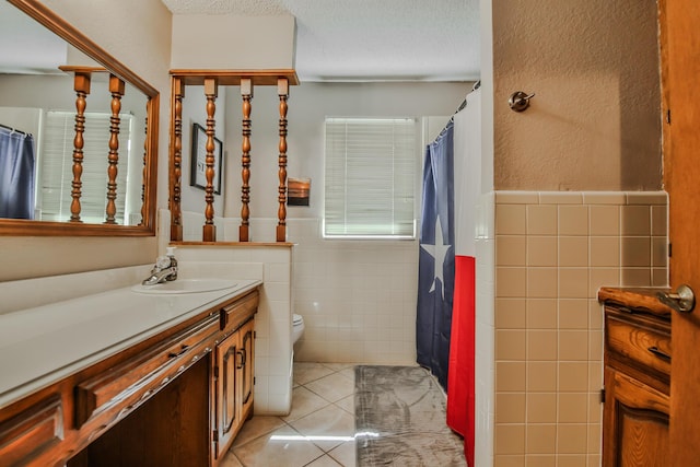 bathroom featuring tile patterned floors, tile walls, toilet, vanity, and a textured ceiling