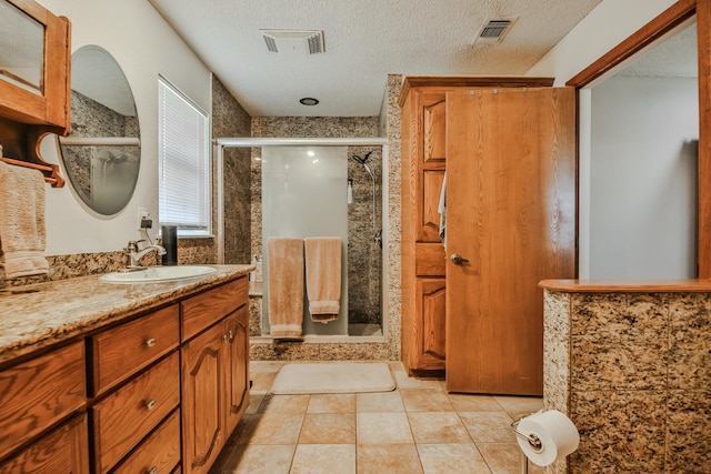 full bath with a stall shower, a textured ceiling, visible vents, and vanity