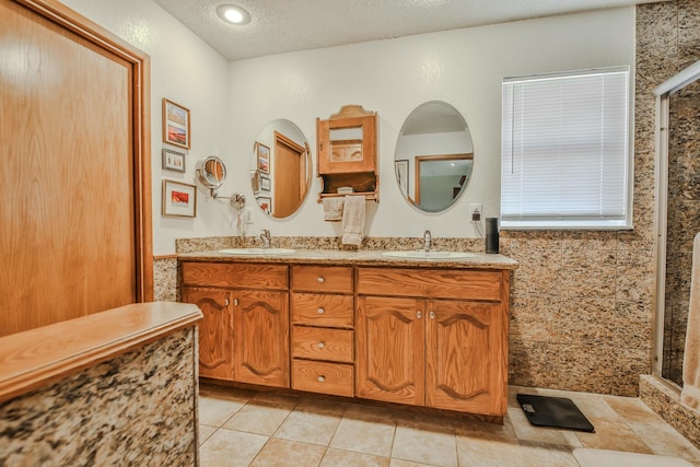 full bath with double vanity, a textured ceiling, tile patterned floors, and a sink