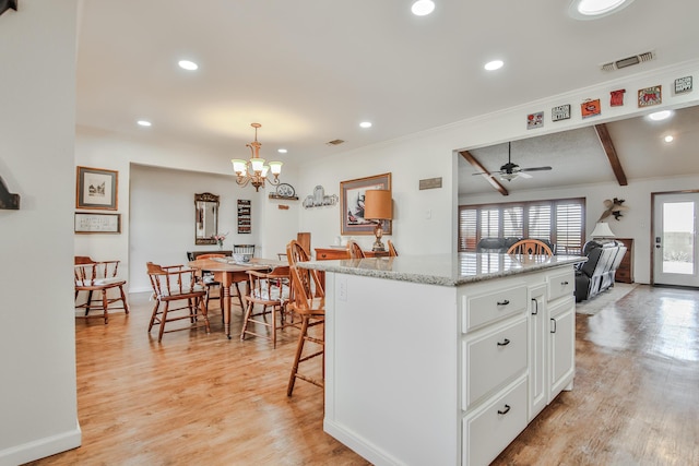 kitchen with light wood-type flooring, a center island, a breakfast bar, white cabinets, and ceiling fan with notable chandelier