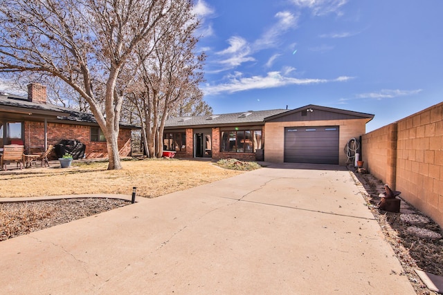 ranch-style home featuring brick siding, a chimney, concrete driveway, an attached garage, and fence