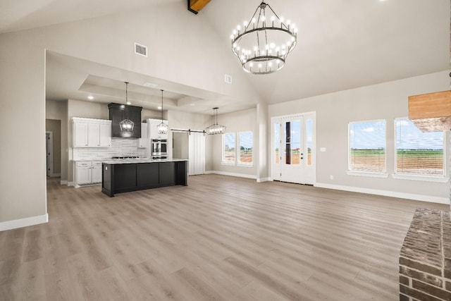 unfurnished living room featuring a barn door, high vaulted ceiling, light wood-type flooring, and a chandelier