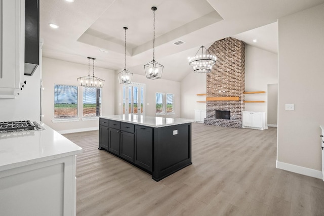 kitchen featuring a center island, hanging light fixtures, a tray ceiling, a fireplace, and light hardwood / wood-style floors