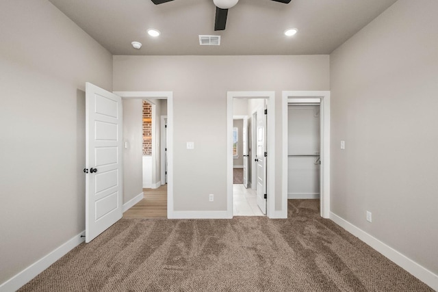 unfurnished bedroom featuring ceiling fan, ensuite bathroom, light carpet, a walk in closet, and a closet