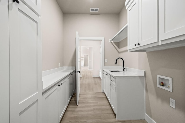 laundry area featuring sink, hookup for a washing machine, light hardwood / wood-style flooring, and cabinets