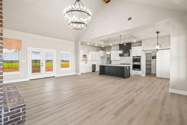 unfurnished living room featuring high vaulted ceiling, light wood-type flooring, a chandelier, and french doors