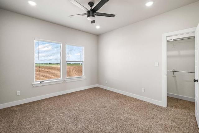 unfurnished bedroom with a walk in closet, a closet, ceiling fan, and carpet flooring