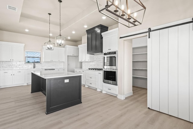 kitchen featuring hanging light fixtures, a kitchen island, a raised ceiling, white cabinets, and a barn door