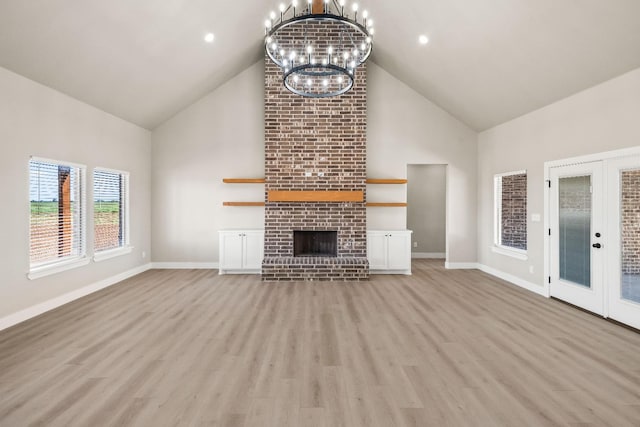 unfurnished living room featuring french doors, high vaulted ceiling, light hardwood / wood-style flooring, a notable chandelier, and a fireplace