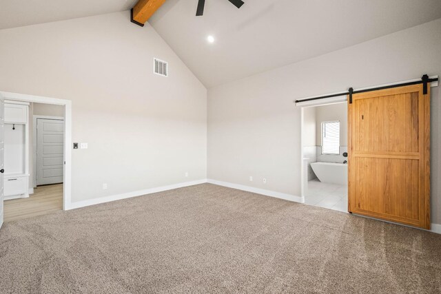 unfurnished bedroom with high vaulted ceiling, beamed ceiling, light colored carpet, a barn door, and ensuite bath