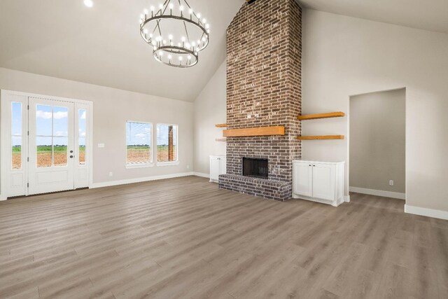 unfurnished living room with light hardwood / wood-style floors, high vaulted ceiling, a brick fireplace, and a notable chandelier