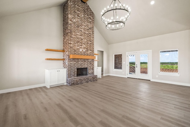 unfurnished living room with french doors, an inviting chandelier, high vaulted ceiling, a brick fireplace, and light hardwood / wood-style floors