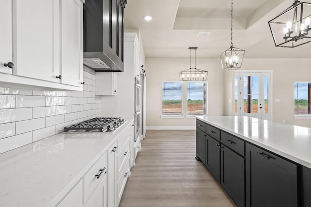 kitchen with stainless steel appliances, a tray ceiling, decorative backsplash, white cabinets, and decorative light fixtures