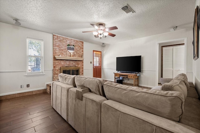 living room with ceiling fan, dark hardwood / wood-style flooring, a brick fireplace, and a textured ceiling