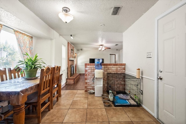 tiled dining room with ceiling fan, a brick fireplace, and a textured ceiling