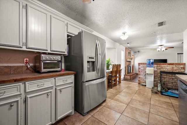 kitchen with dishwasher, stainless steel fridge, light tile patterned floors, a brick fireplace, and a textured ceiling