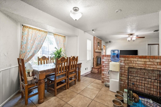 dining room with a brick fireplace, tile patterned floors, a textured ceiling, and ceiling fan