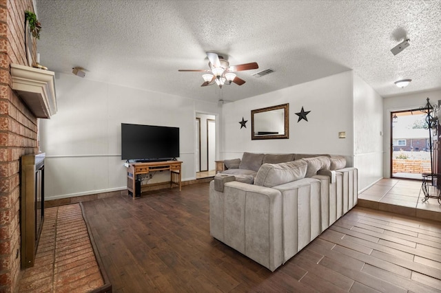 living room with a brick fireplace, a textured ceiling, dark hardwood / wood-style floors, and ceiling fan