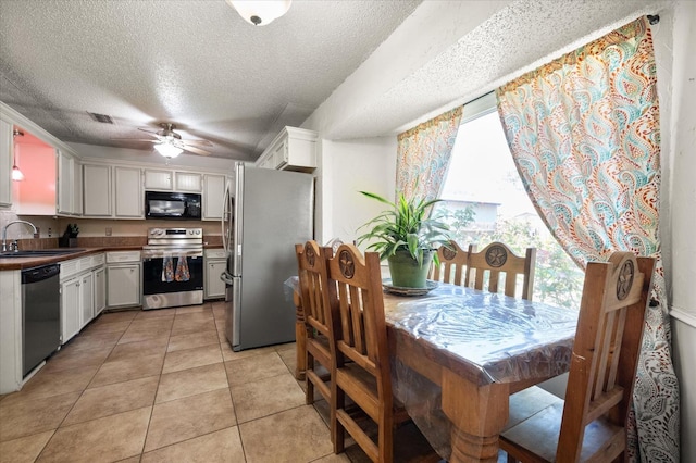 kitchen with appliances with stainless steel finishes, white cabinetry, sink, light tile patterned floors, and ceiling fan