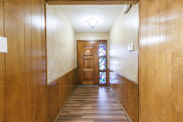 doorway with dark wood-type flooring, wooden walls, and a textured ceiling