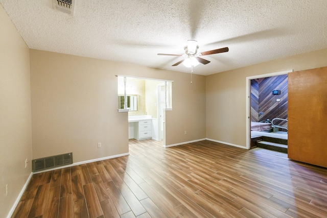 unfurnished room featuring wood-type flooring, built in desk, a textured ceiling, and ceiling fan