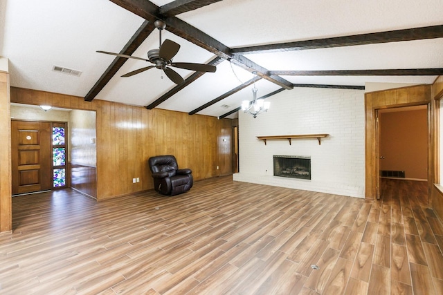 unfurnished living room with ceiling fan with notable chandelier, a fireplace, wood walls, lofted ceiling with beams, and wood-type flooring