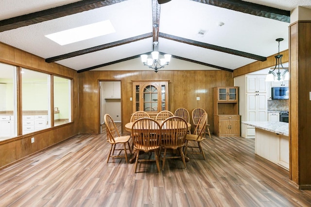 dining space featuring a notable chandelier, lofted ceiling with beams, wood walls, and light wood-type flooring