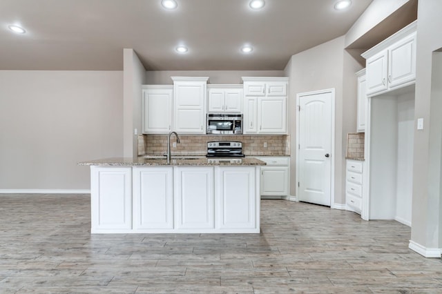 kitchen featuring sink, white cabinets, stainless steel appliances, light stone countertops, and a center island with sink