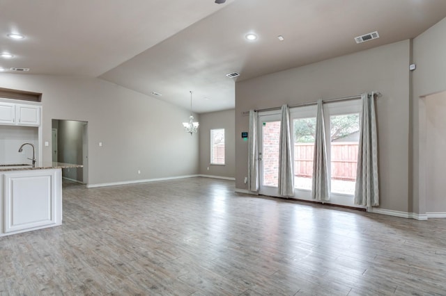 unfurnished living room featuring vaulted ceiling, sink, light wood-type flooring, and a notable chandelier