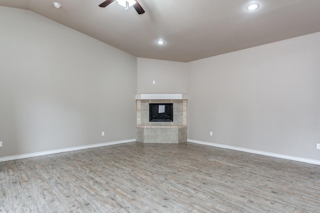 unfurnished living room with a tile fireplace, vaulted ceiling, ceiling fan, and light hardwood / wood-style flooring