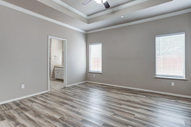 empty room with crown molding, light hardwood / wood-style flooring, a raised ceiling, and ceiling fan