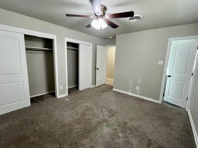 unfurnished bedroom featuring multiple closets, dark colored carpet, and ceiling fan